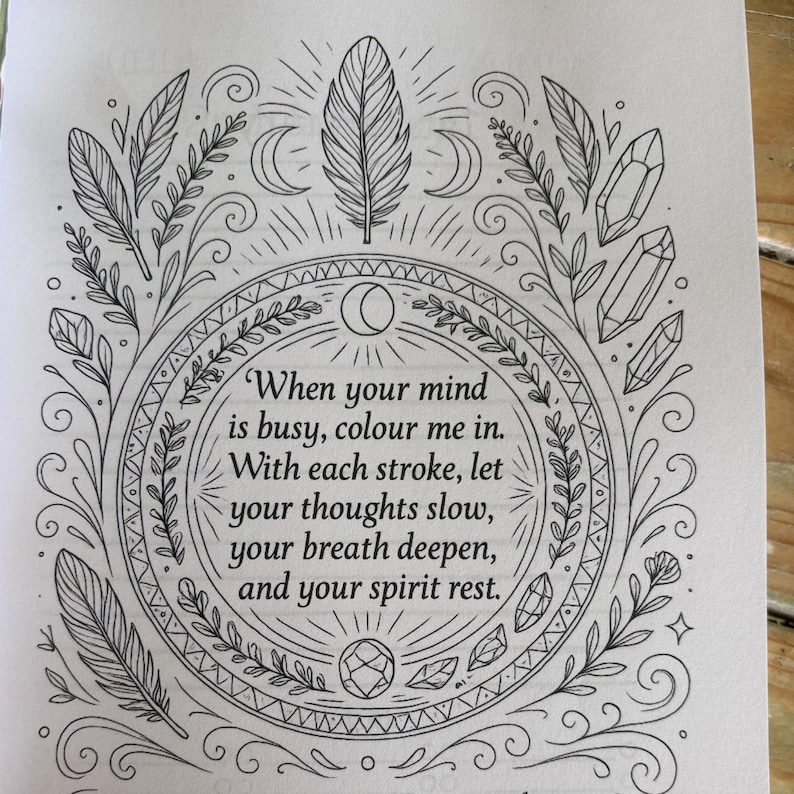 K&ouml;nnte beinhalten: Schwarz-Wei&szlig;-Illustration mit Text. Das Design zeigt einen kreisf&ouml;rmigen Rahmen mit Federn, Kristallen und Halbmonden. Der Text lautet: &bdquo;Wenn dein Geist besch&auml;ftigt ist, male mich aus. Mit jedem Strich lass deine Gedanken langsamer werden, deinen Atem tiefer werden und deinen Geist ruhen."