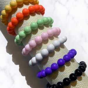 May include: A stack of colorful silicone beaded bracelets in yellow, orange, green, pink, white, purple, and black.
