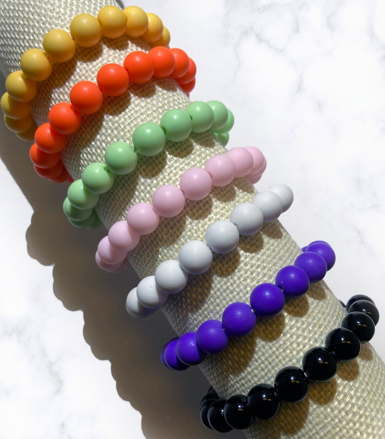 May include: A stack of colorful silicone beaded bracelets in yellow, orange, green, pink, white, purple, and black.