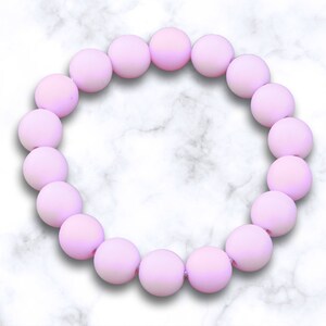 May include: A pink beaded bracelet with a matte finish. The bracelet is made of round beads and is strung on a clear elastic cord.