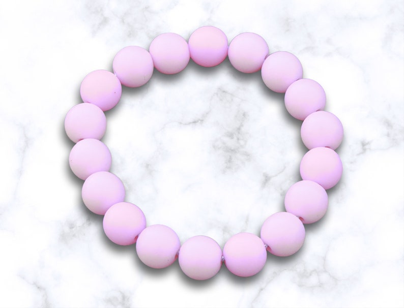 May include: A pink beaded bracelet with a matte finish. The bracelet is made of round beads and is strung on a clear elastic cord.