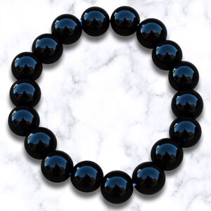 May include: A black beaded bracelet with shiny, round beads. The bracelet is made of natural black onyx stones.