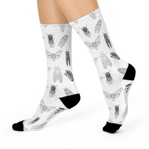 May include: White socks with a black and white pattern of cicadas. The socks are shown on a model's feet.