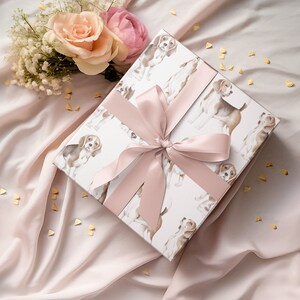 May include: A white gift box with a pink ribbon and a pattern of brown and white dogs. The box is on a pink fabric background with gold confetti.