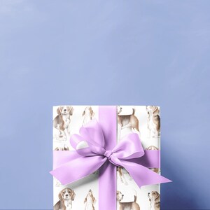 May include: A white gift box with a purple ribbon and a pattern of beagle dogs. The box is sitting on a light blue surface.