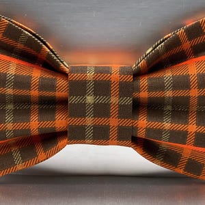 May include: A plaid bow tie in shades of orange and brown. The bow tie features a classic plaid pattern with a repeating square design. The bow tie is a stylish accessory for formal or casual wear.
