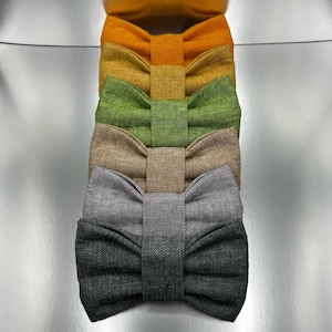 May include: A vertical stack of five bow ties made from a textured fabric. The colors from top to bottom are bright orange, golden yellow, grass green, light tan, and two shades of gray, ranging from a light heather gray to a dark charcoal gray.