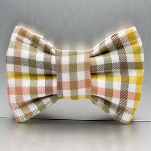 May include: A fabric bow tie with a gingham check pattern in white, yellow, pink, green, and brown. The bow tie is knotted in the centre, and would be suitable for a formal occasion.