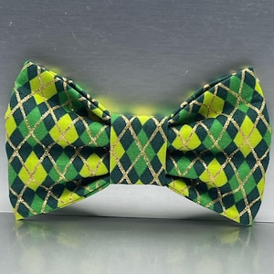 May include: A green and yellow bow tie with a diamond pattern and gold accents. The bow tie is made of fabric and is designed to be worn around the neck. The bow tie is a fashion accessory.