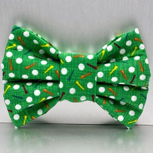 May include: A green bow tie with white golf balls and colorful golf tees printed on it.