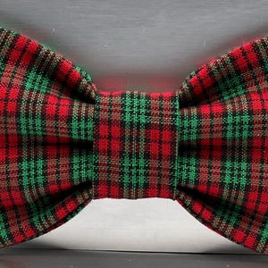 May include: A red, green, and black plaid bow tie. The bow tie is made of fabric and has a classic bow shape. The plaid pattern is a traditional design, with red as the primary color, accented by green and black.