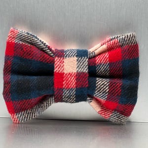 May include: A red, black and white plaid bow tie. The bow tie is made of a soft, fuzzy fabric.