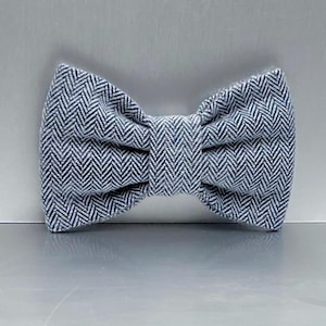 May include: A gray and white herringbone patterned bow tie. The bow tie is made of fabric and has a classic shape. The fabric has a textured appearance and is folded in the center.