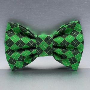 May include: A green and black plaid bow tie. The bow tie features a repeating diamond pattern in shades of green and black, with small yellow accents. The bow tie is a classic accessory.