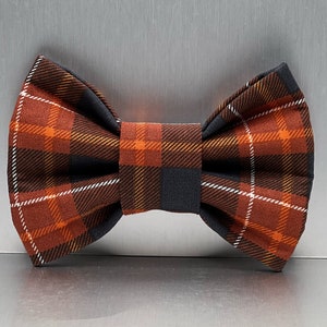 May include: A brown, orange, and black plaid bow tie. The bow tie is made of a soft, comfortable fabric and has a classic bow shape.