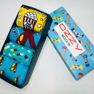May include: A blue box containing four pairs of colourful socks. The socks feature various designs, including popcorn, chips, pills, and trucks. The box is labelled "OzZy Socks" and "4 Pairs".