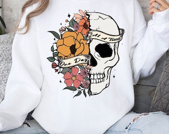 May include: White sweatshirt with a floral and skull design. The skull is half floral and half bone. The text on the banner reads "One Day at a Time".