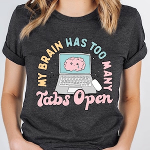 May include: A dark gray t-shirt with a graphic of a laptop with a brain inside. The text on the shirt reads "My brain has too many tabs open".