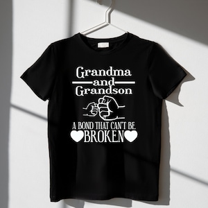 May include: Black t-shirt with white text that reads "Grandma and Grandson" with a fist bump graphic and "A bond that can't be broken" with two hearts.