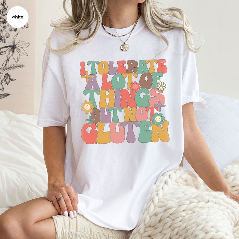 May include: White t-shirt with a graphic that says "I tolerate a lot of things but not gluten" in colorful, retro-style lettering.