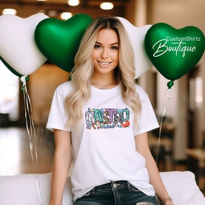 K&ouml;nnte beinhalten: Ein wei&szlig;es T-Shirt mit einem bunten Grafikdesign, auf dem "Castro Crew" steht. Das Design enth&auml;lt eine Vielzahl von Mustern, darunter Tiermuster, Blumenmuster und geometrische Muster. Das Shirt wird von einer Person mit langen blonden Haaren getragen.