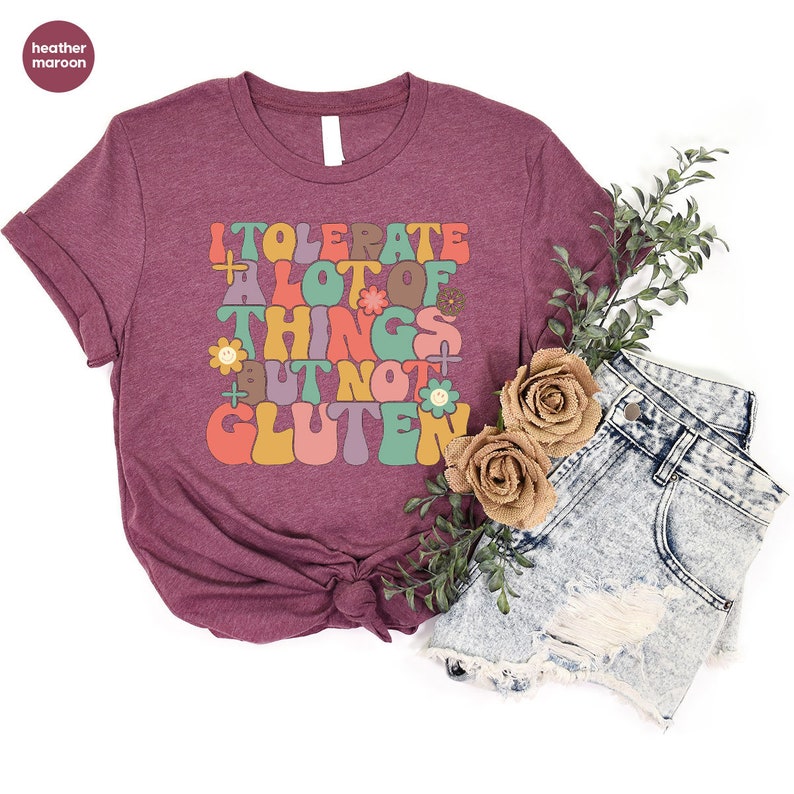 May include: A maroon t-shirt with the text "I tolerate a lot of things but not gluten" in a retro font with colorful flowers and smiley faces.