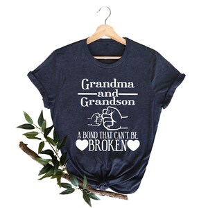 May include: A navy blue t-shirt with white text that reads "Grandma and Grandson" with a fist bump graphic and the text "A bond that can't be broken" with two hearts.