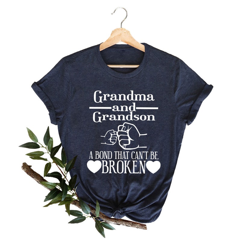 May include: A navy blue t-shirt with white text that reads "Grandma and Grandson" with a fist bump graphic and the text "A bond that can't be broken" with two hearts.