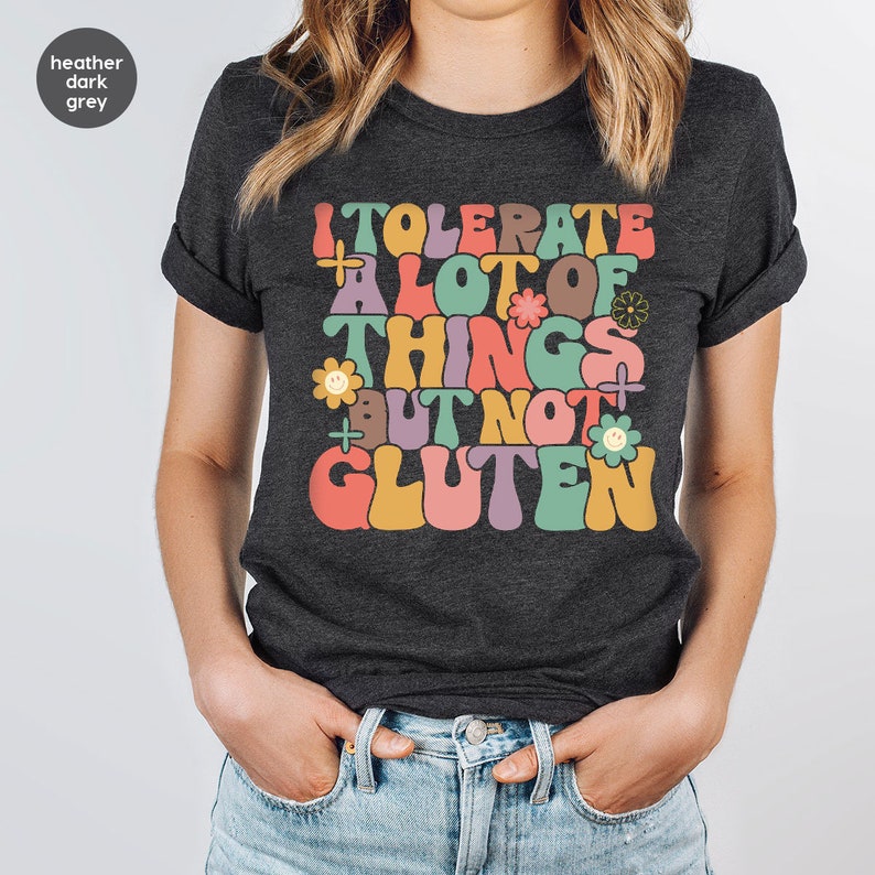 May include: Heather dark grey t-shirt with a retro-style graphic that says "I tolerate a lot of things but not gluten". The graphic features colorful letters, flowers, and smiley faces.