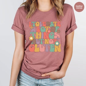 May include: A heather mauve t-shirt with a retro-style graphic that reads "I tolerate a lot of things but not gluten".