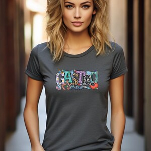 K&ouml;nnte beinhalten: Ein dunkelgraues T-Shirt mit einem bunten Grafikdesign, auf dem "Gastro Crew" steht. Die Grafik enth&auml;lt verschiedene medizinische Symbole und Muster.