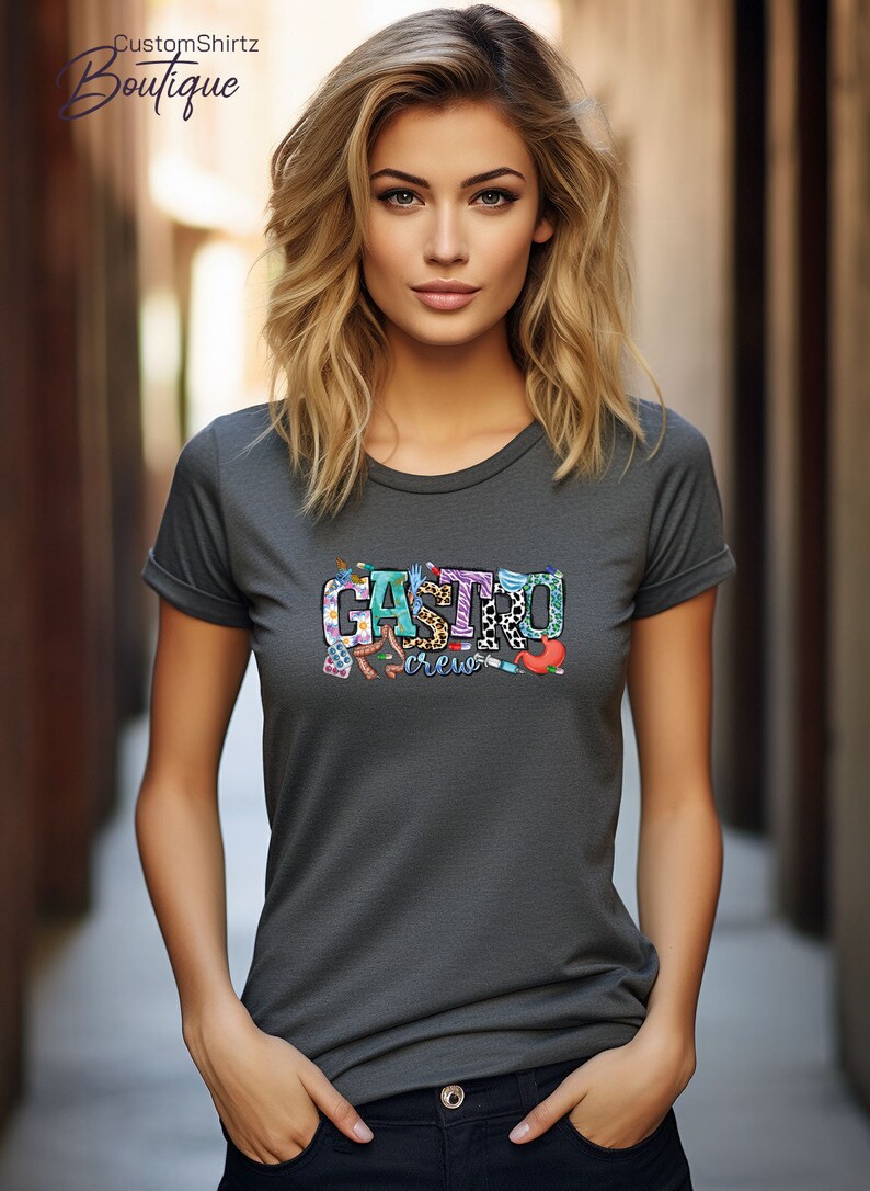 K&ouml;nnte beinhalten: Ein dunkelgraues T-Shirt mit einem bunten Grafikdesign, auf dem "Gastro Crew" steht. Die Grafik enth&auml;lt verschiedene medizinische Symbole und Muster.