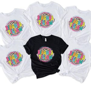 May include: A selection of white and black t-shirts. Each shirt displays a vibrant graphic with the words "DIAGNOSTICIAN" in a fun font, encircled by a leopard print design and a pink and blue ring.