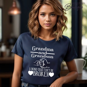 May include: A navy blue t-shirt with white text that reads "Grandma and Grandson" with a fist bump graphic and the text "A bond that can't be broken" with two white hearts.