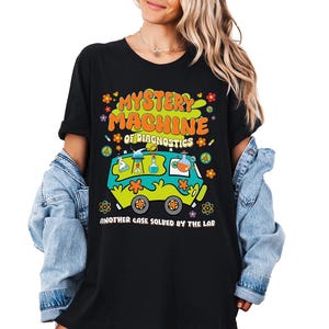 May include: Black t-shirt with a retro-style graphic of a van with the text "Mystery Machine of Diagnostics" and "Another Case Solved by the Lab".