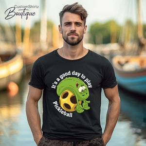 May include: A black t-shirt with a green pickleball character and the text "It's a good day to play Pickleball".