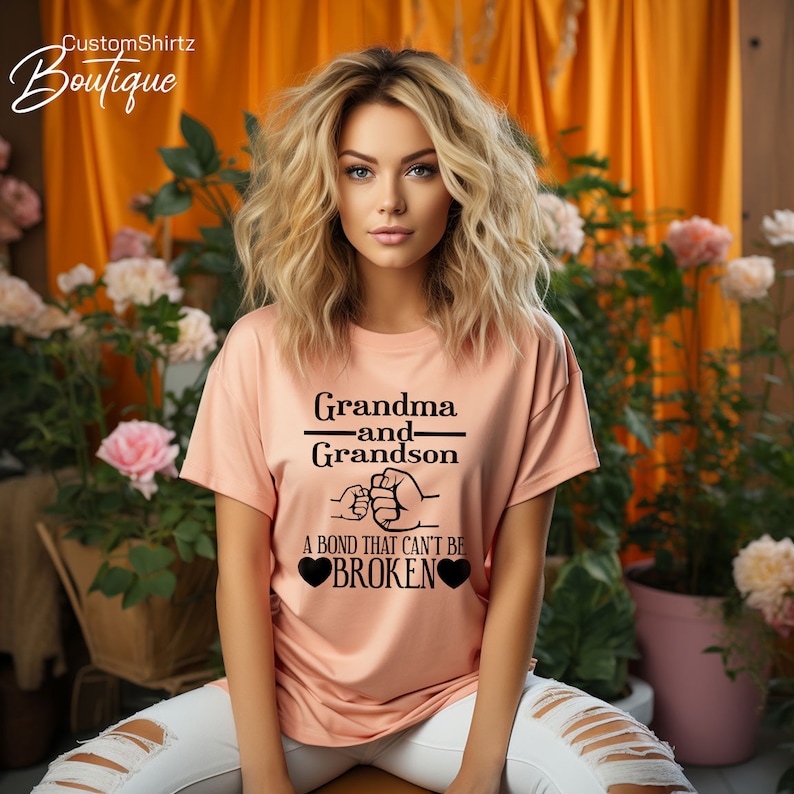 May include: A peach-colored t-shirt with a black graphic that reads "Grandma and Grandson" with a fist bump design and the text "A bond that can't be broken" with two black hearts.