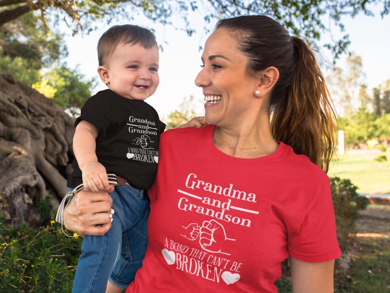 May include: A red and black matching set of t-shirts for a grandma and grandson. The shirts feature the text "Grandma and Grandson" with a fist bump graphic and the text "A bond that can't be broken".