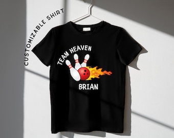 Op de afbeelding: Zwart T-shirt met een witte afbeelding van bowlingpinnen en een bowlingbal in brand. De tekst "Team Heaven" en "Brian" staan op het shirt gedrukt.