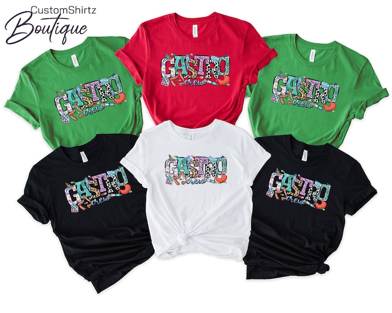 K&ouml;nnte beinhalten: F&uuml;nf T-Shirts in verschiedenen Farben mit dem Text "Gastro Crew" in bunten Buchstaben. Die Shirts sind gr&uuml;n, rot, wei&szlig;, schwarz und dunkelgrau.
