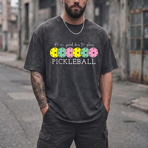 A man wearing a gray t-shirt with a graphic design of colorful pokleball balls printed on it.