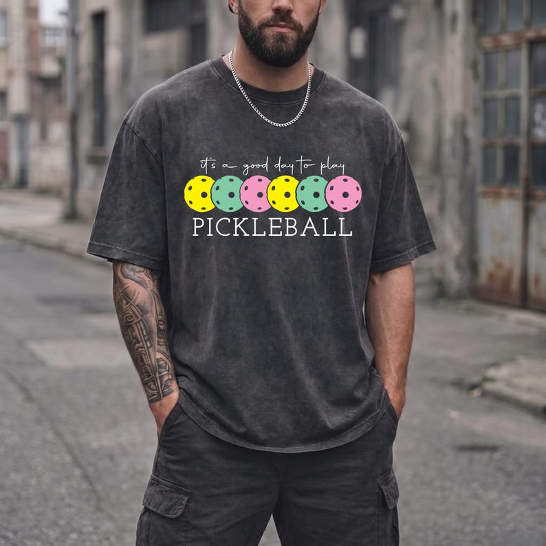 A man wearing a gray t-shirt with a graphic design of colorful pokleball balls printed on it.