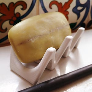 Peut inclure: Un porte-savon blanc avec un design ondulé contient une barre de savon vert clair.