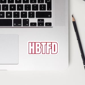 May include: A white laptop with a red sticker that says "HBTFD" on the top right corner of the laptop.