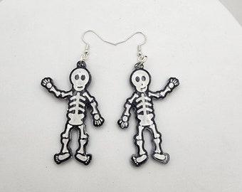 May include: A pair of silver skeleton earrings. Each earring features a white skeleton with black outlines, and a silver hook.