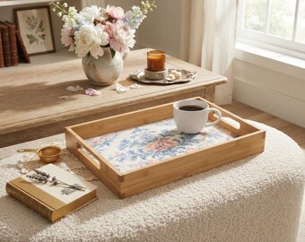Può includere: Un vassoio da portata rettangolare in bambù con manici intagliati e una base con motivo floreale. Il vassoio presenta una finitura in legno chiaro e contiene una tazza in ceramica bianca riempita di caffè nero, appoggiato su un pouf color crema.