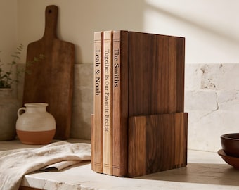 Può includere: Un set di tre taglieri in legno disposti verticalmente in un supporto in legno abbinato. I bordi stretti dei taglieri presentano incisioni con i testi The Smiths, Together Is Our Favorite Recipe e Leah & Noah.