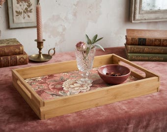 Può includere: Un vassoio da portata rettangolare in bambù con una base a motivo floreale nei toni del rosa, crema e verde. Il vassoio è dotato di manici laterali integrati e contiene un calice in vetro intagliato con un fiore secco e una ciotola rosa opaco.