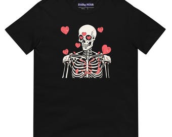 Puede incluir: Camiseta negra con un gráfico de esqueleto que lleva gafas en forma de corazón y rodeado de corazones rosas. El texto "DARQ-NOIR" está impreso en la camiseta.