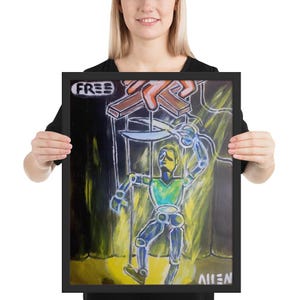 May include: A framed painting of a puppet with a blue body and green shirt. The puppet is being cut free from strings by a pair of scissors. The painting is on a black background with yellow and orange highlights. The word "FREE" is written in black on a white background in the top left corner of the painting. The word "ALIEN" is written in black on a white background in the bottom right corner of the painting.